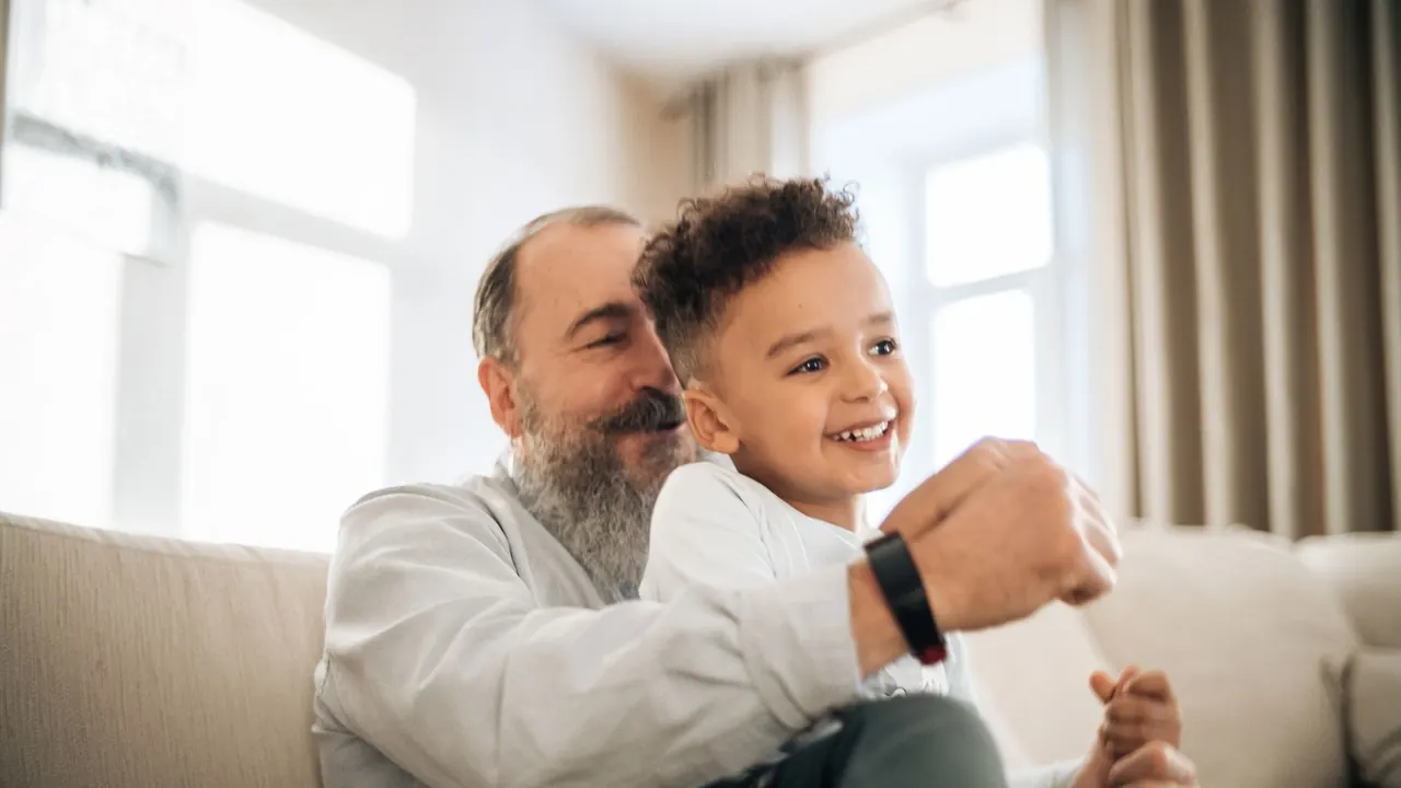 grandfather laughing with his grandson on the sofa, image for turning 60 humor