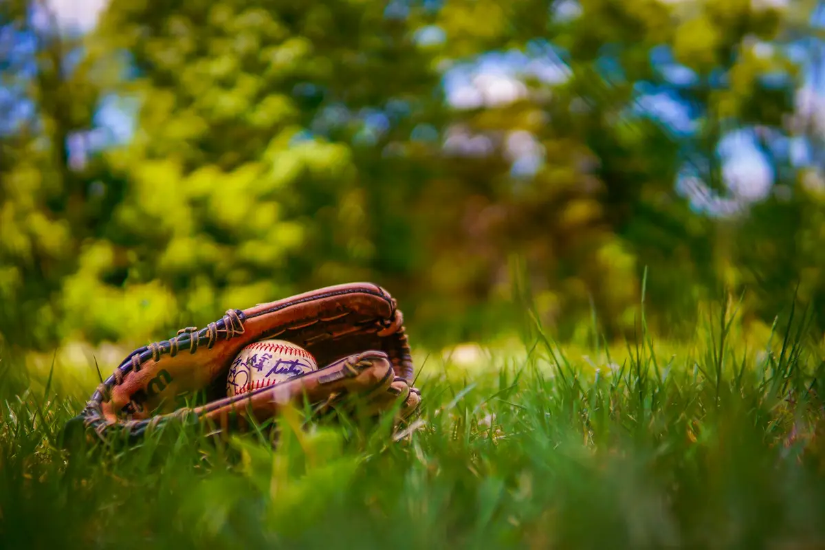 small baseball glove with a ball resting in green grass, scene for baseball puns for kids