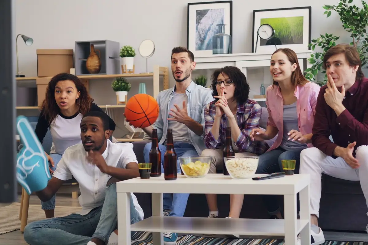 group of friends cheering while watching a game on TV with snacks, march madness jokes