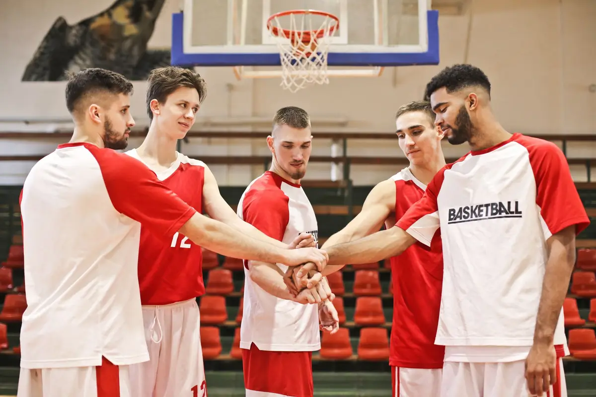 basketball team stacking hands in a huddle in a gym, funny basketball jokes for game day