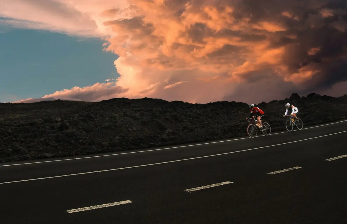 rider on a bike crossing an empty road under orange sunset clouds, image for bike puns for instagram captions