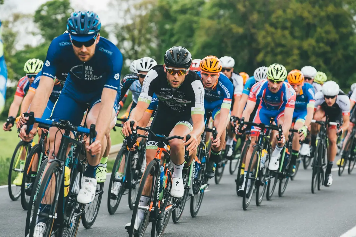 group of riders in helmets racing side by side on an open road, image for bike race puns