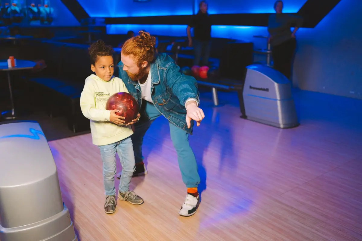 father teaching his young son to bowl at an indoor bowling alley, bowling jokes for kids