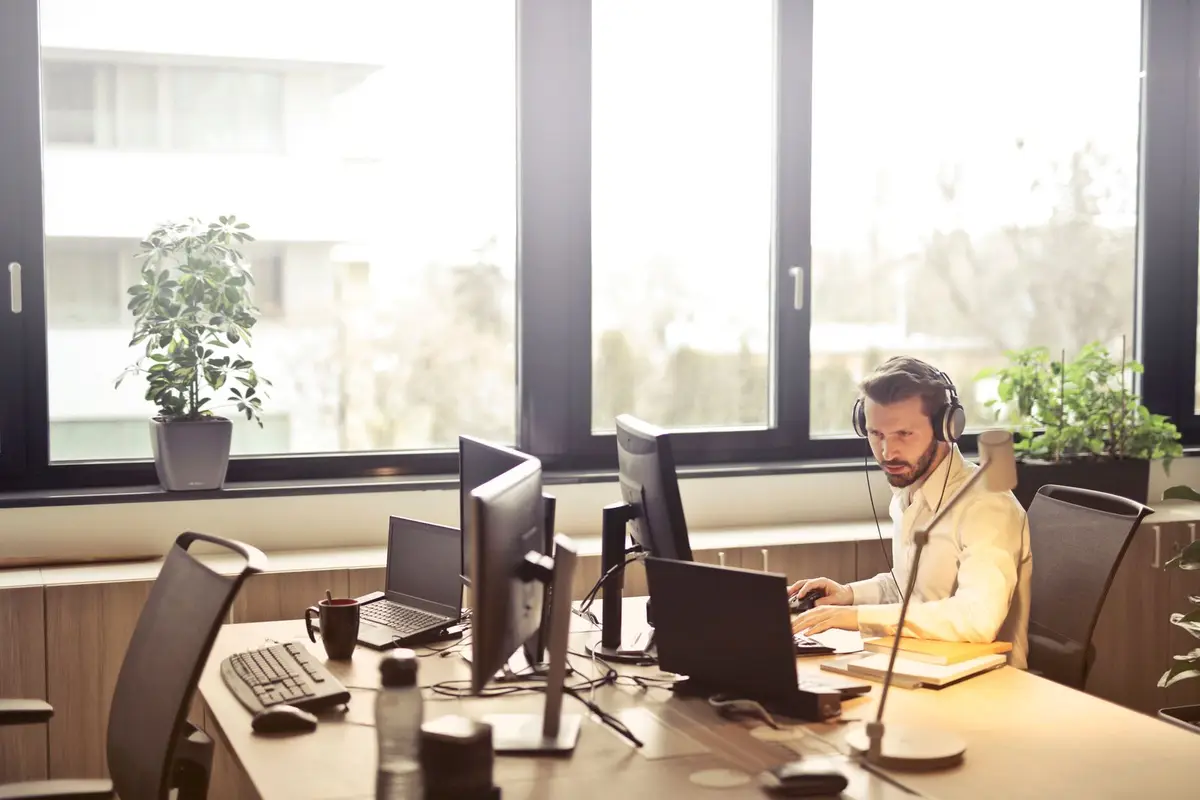IT worker with a headset at a desk with several computer monitors, IT jokes for work