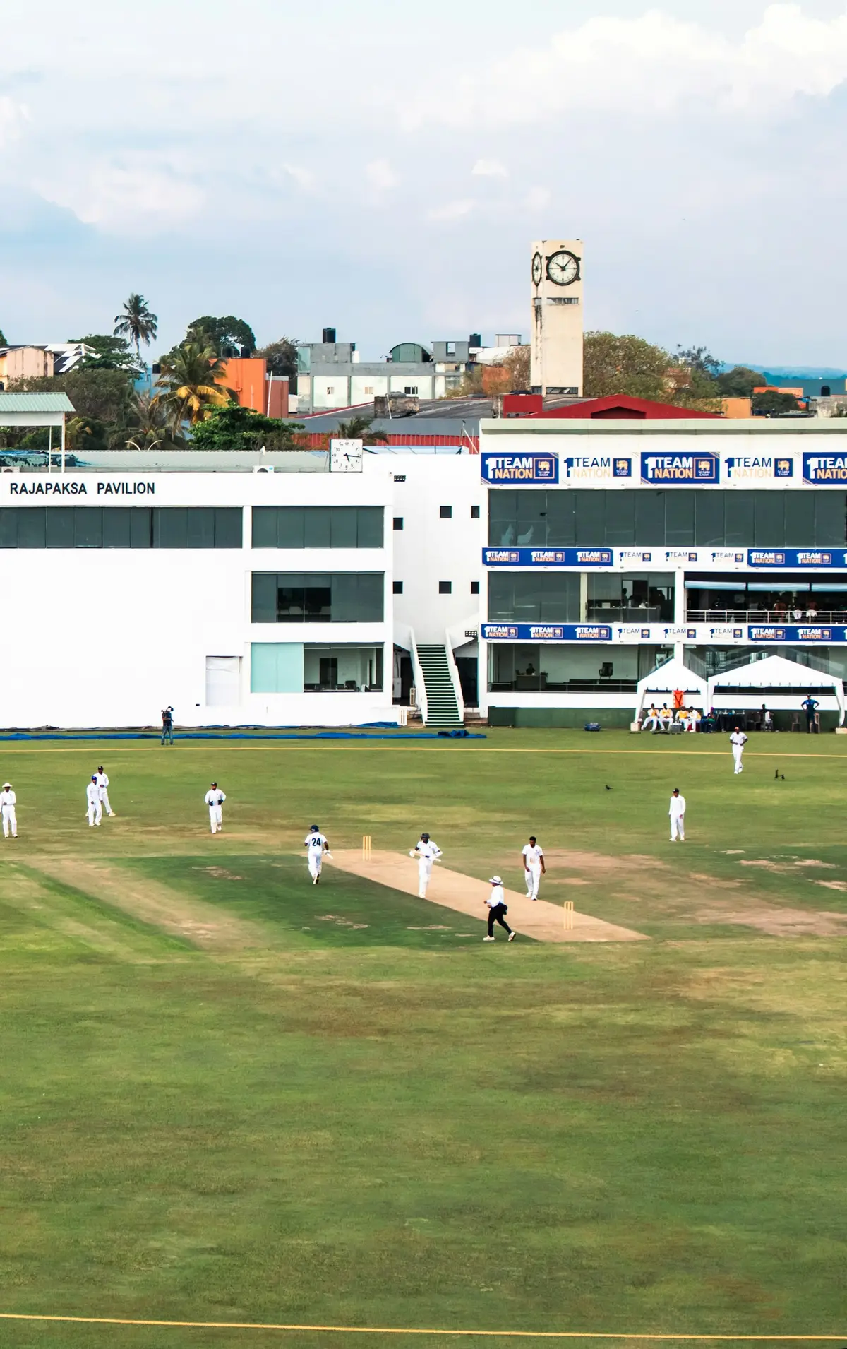 cricket match happening on a green field with players in white, scene for cricket puns one liners