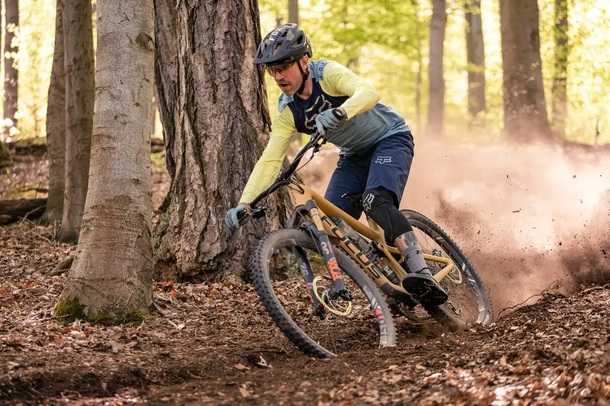 mountain biker in a helmet kicking up dirt on a forest trail, image for mountain bike puns