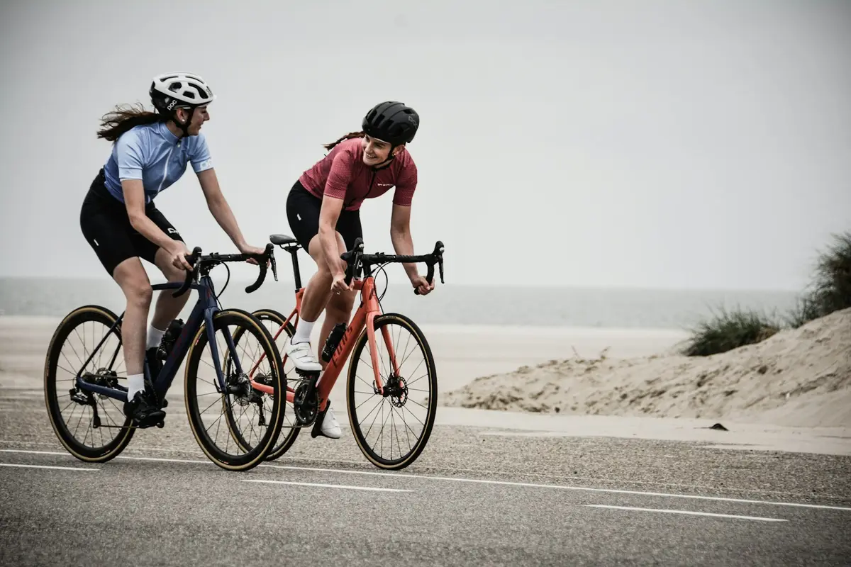 two cyclists in helmets riding road bikes along a seaside road, image for bike puns for instagram captions