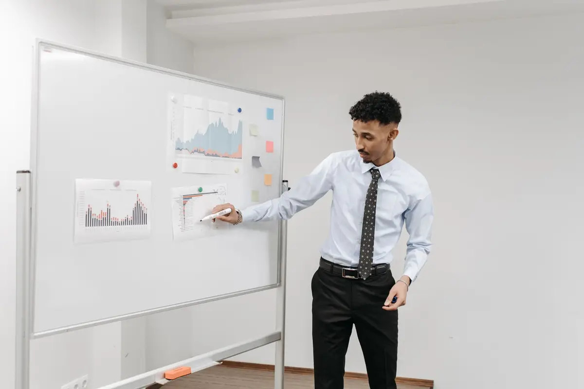 man presenting charts on a whiteboard in an office meeting, data science jokes for the office
