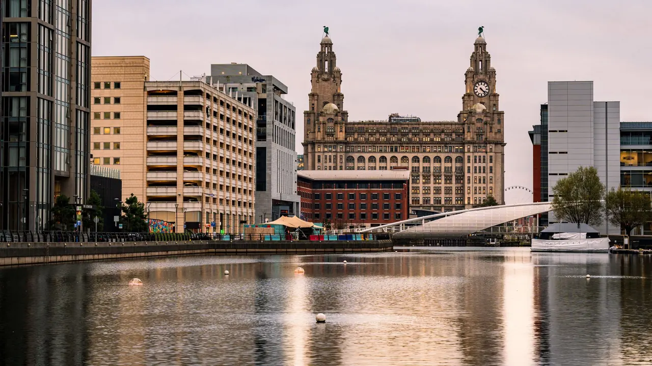 the liverpool waterfront with historic buildings reflected in the water, image for everton jokes about liverpool