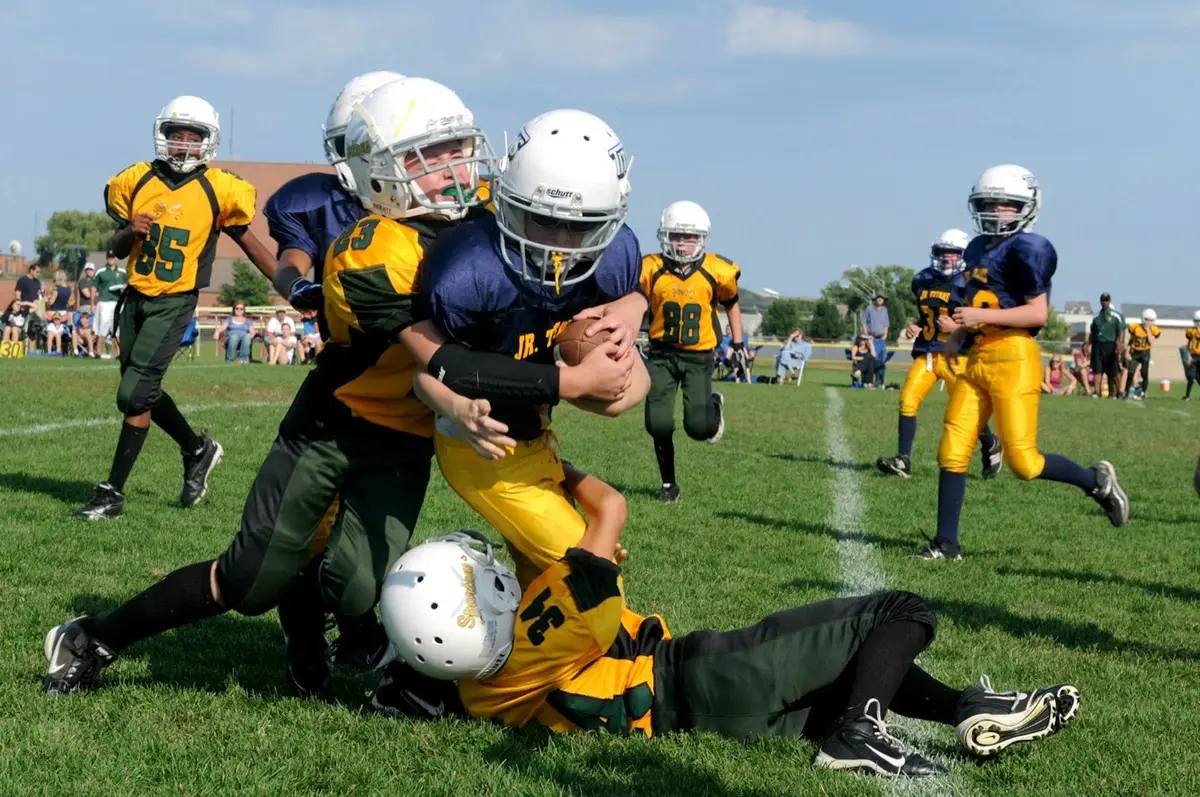 youth football ball carrier wrapped up by defenders during a tackle, image for football position puns about linemen and running backs