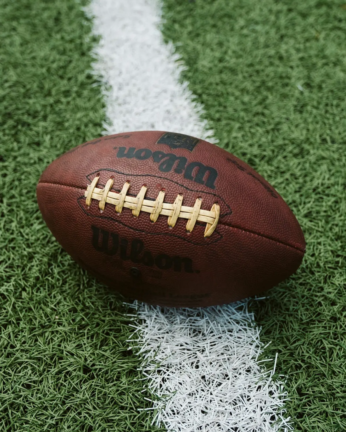 brown American football resting on a white yard line on green turf, ideal for short football puns about touchdowns