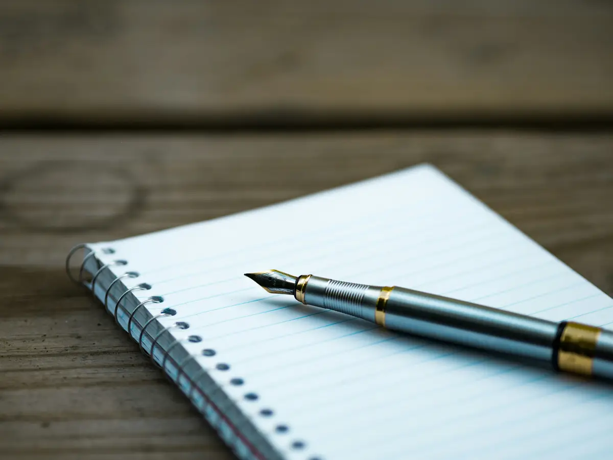 fountain pen resting on an open spiral notebook, scene for writing puns and writer jokes