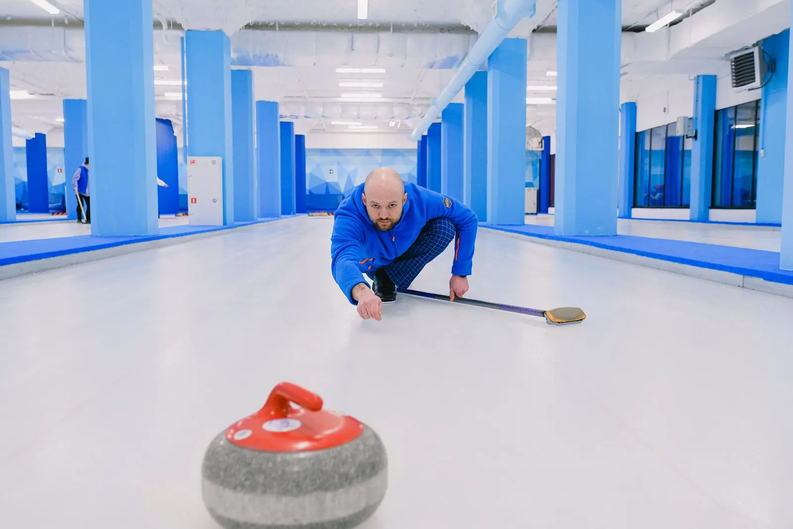 player sliding and throwing a curling stone during a game, image for funny curling jokes for the skip and sweepers