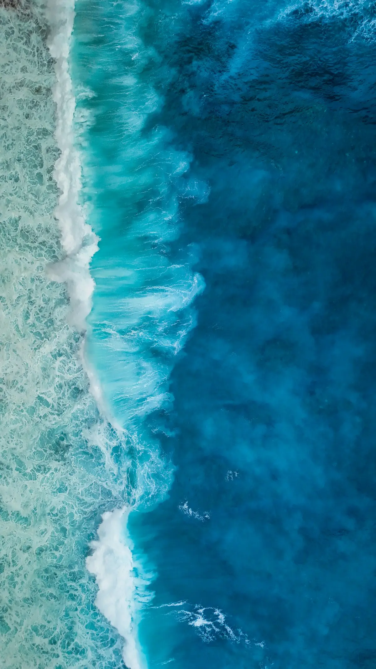 an aerial view of turquoise ocean waves crashing along a coastline, image for ocean and coastline geography puns