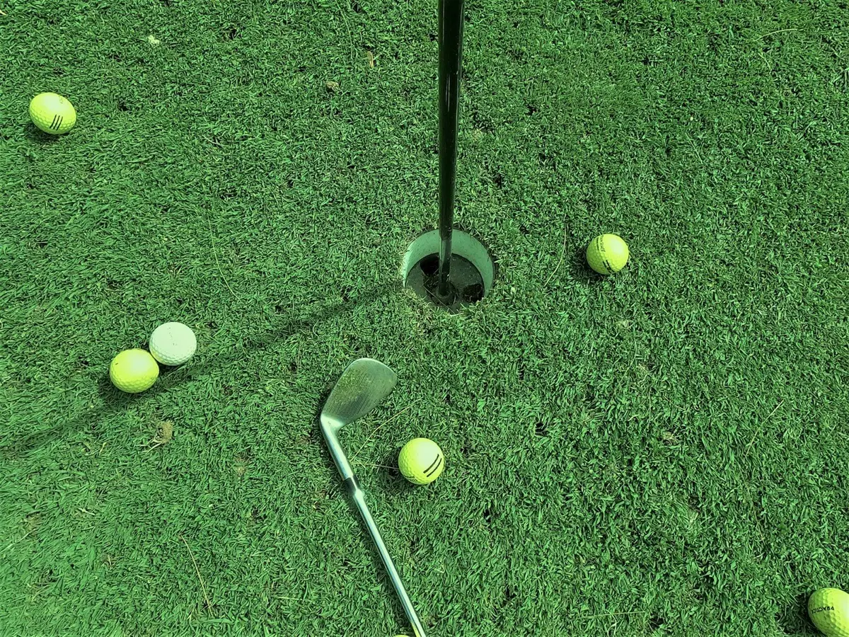 yellow golf balls scattered around a hole on a green with a wedge, image for putting green puns