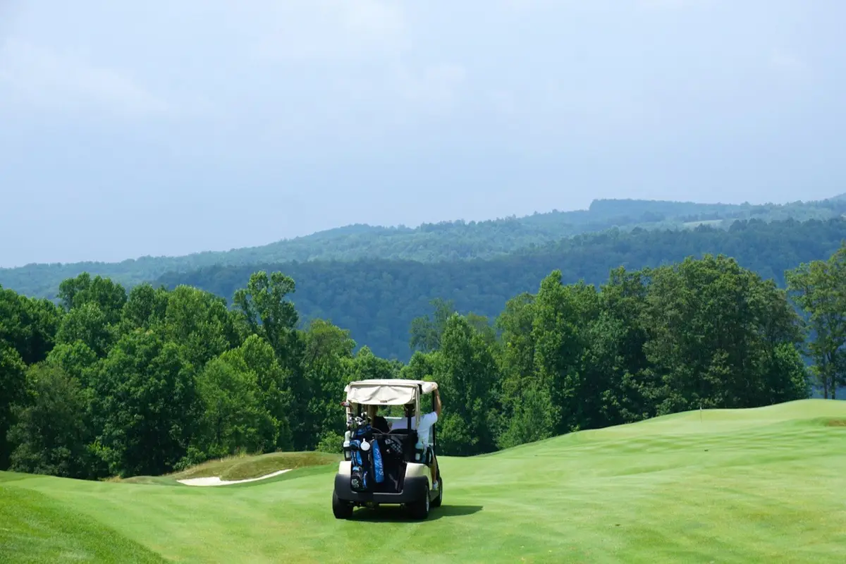 golf cart driving down a green fairway toward mountains, setting for golf cart puns and golf course jokes