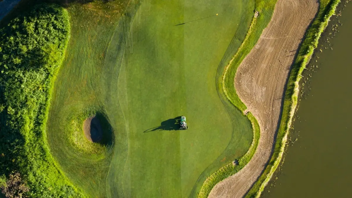 aerial view of a golf green with a bunker and a mower, setting for golf puns about greens and sand traps