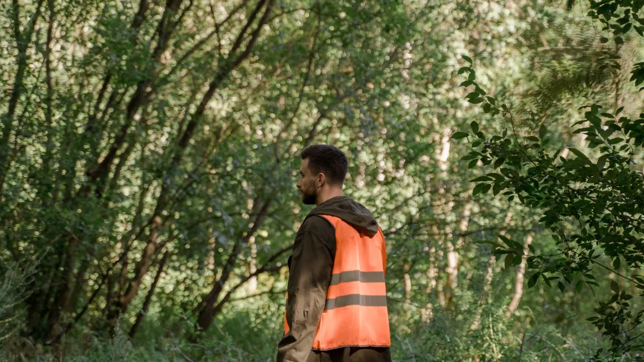 a man in a bright orange safety vest standing in a green forest, image for blaze orange hunting jokes