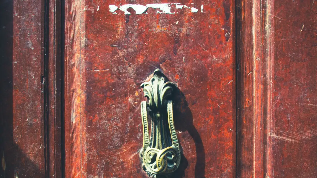 an antique brass door knocker on a red wooden door, image for knock knock running jokes
