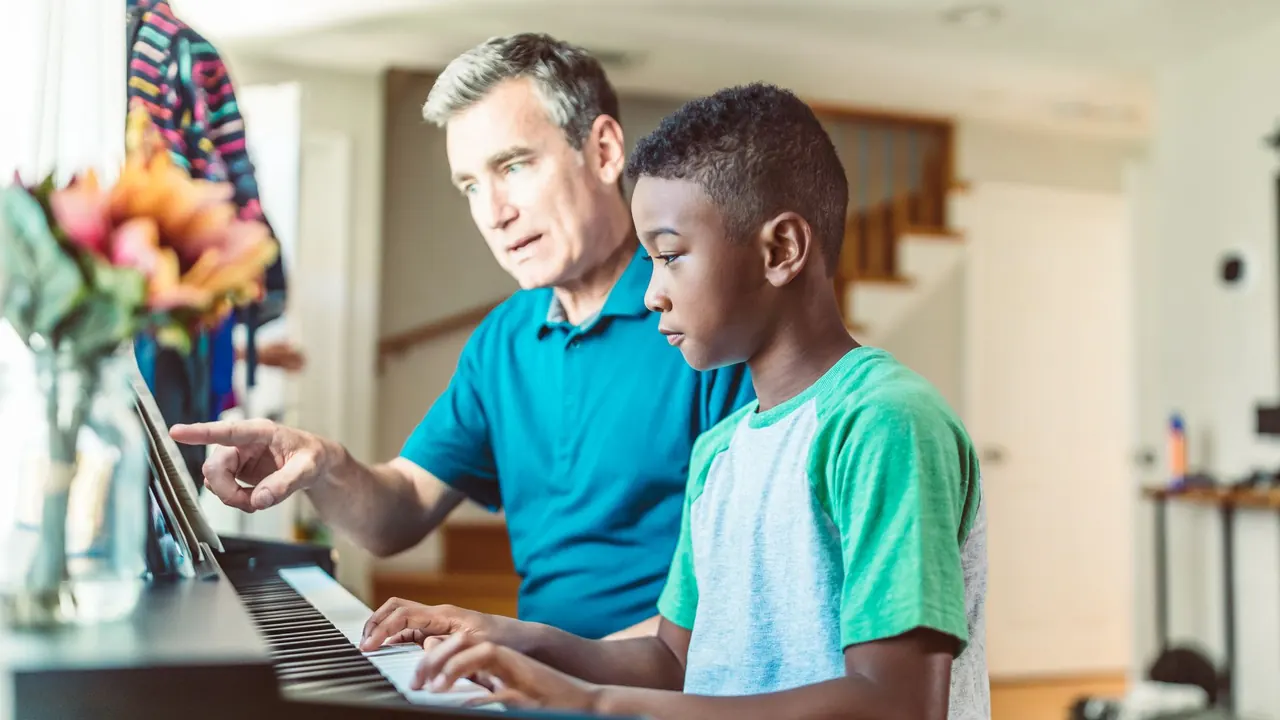 a father teaching his young son to play the piano at home, image for piano dad jokes
