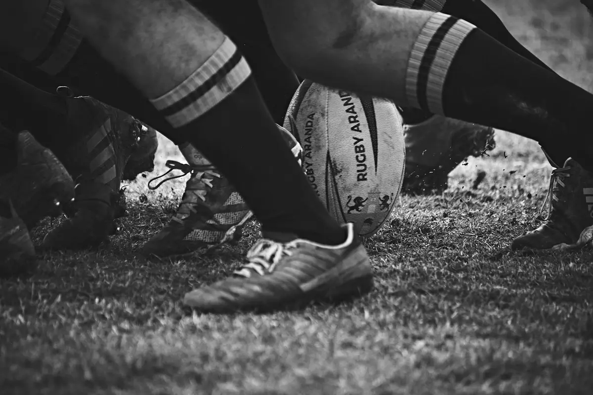 close-up of a rugby ball on the ground beside boots, scene for rugby puns one liners