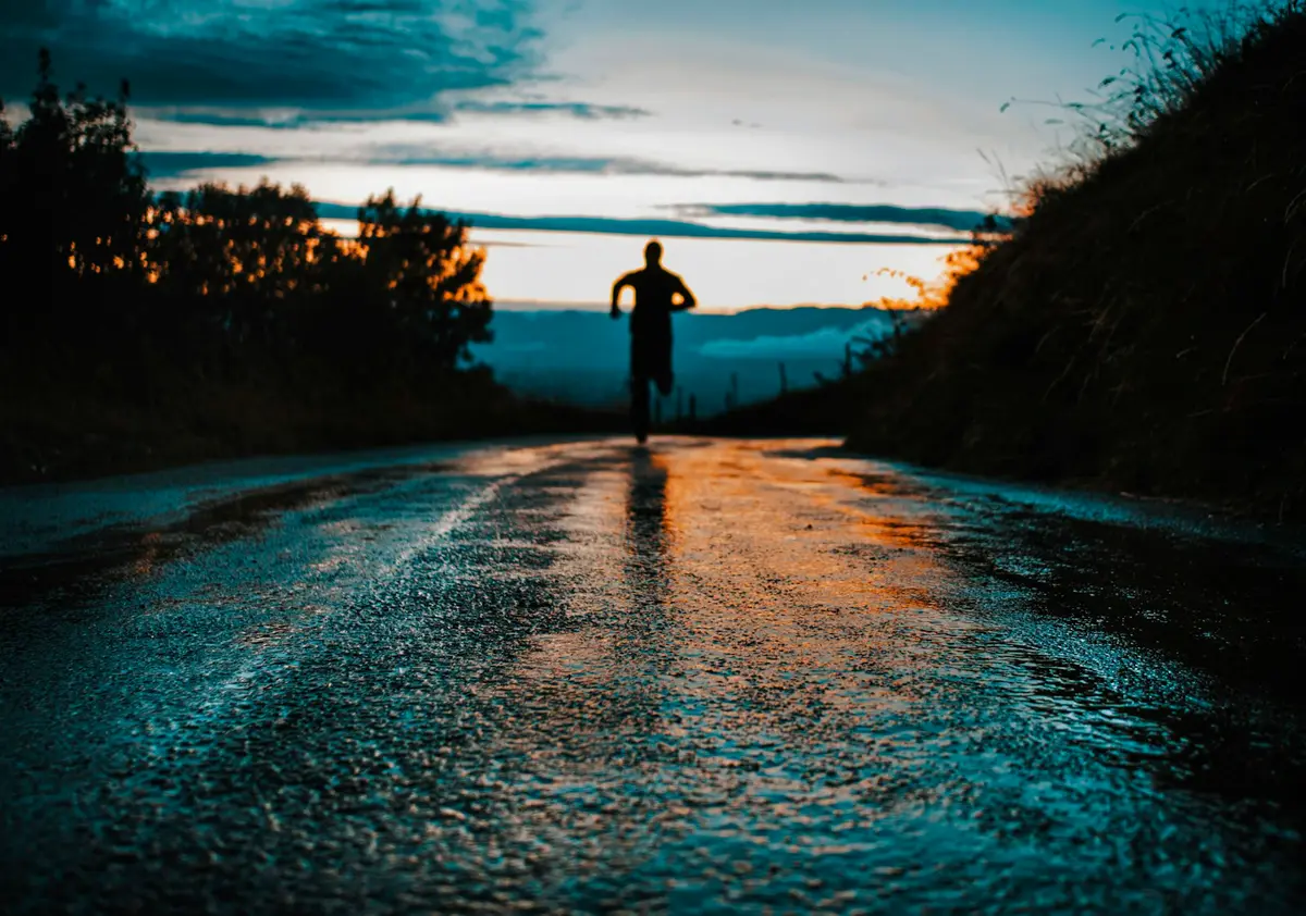 runner silhouetted on a wet country road at dusk, scene for short running puns for instagram