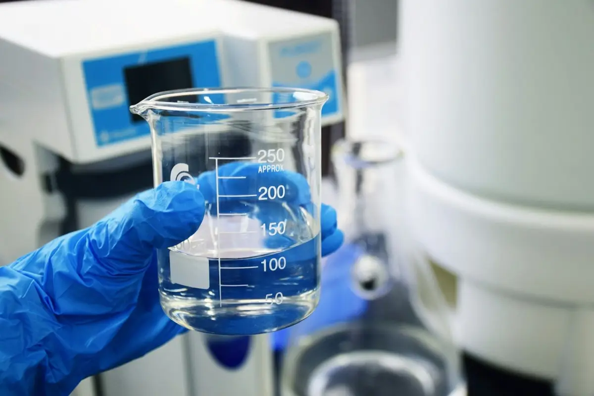 gloved hand holding a glass beaker in a laboratory, an image for chemistry puns and lab captions