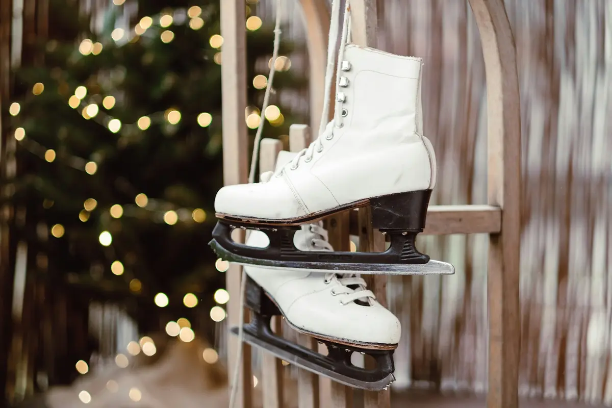 pair of white ice skates hanging on a wooden fence beside holiday string lights, image for skating puns captions