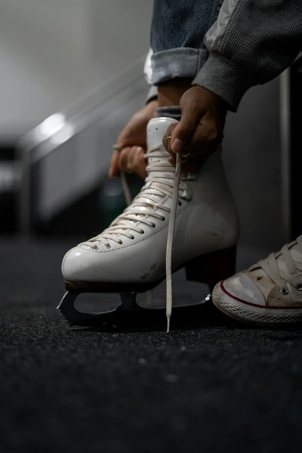 hands lacing a white figure skate next to a canvas sneaker, image for ice skating puns