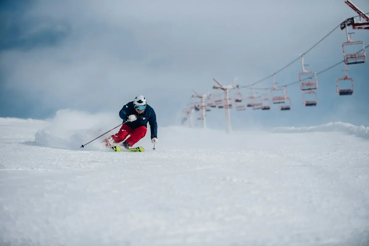 skier carving a turn in powder beneath a row of chairlift chairs, scene for chairlift skiing puns