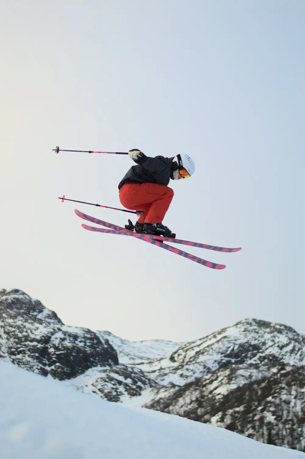 skier crouched mid-air above a snowy ridge with poles out, scene for funny skiing puns