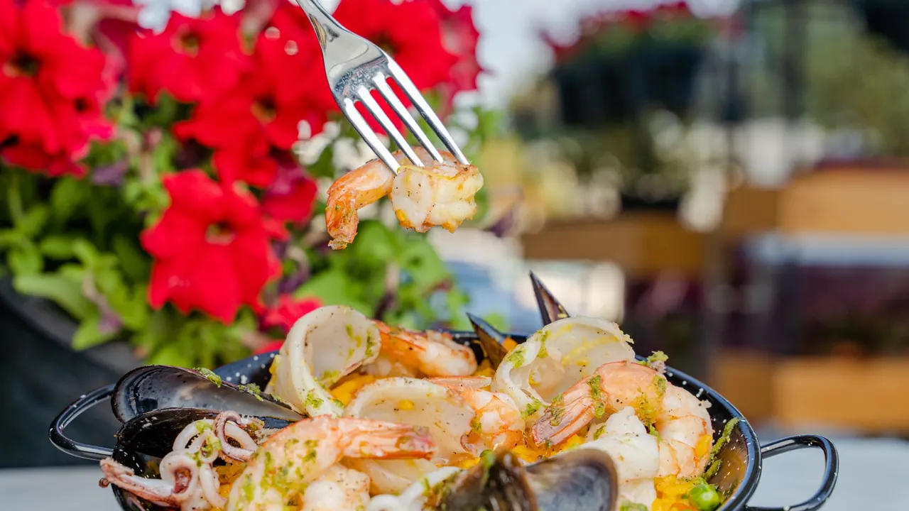 a pan of seafood paella served at an outdoor table, image for spanish food jokes