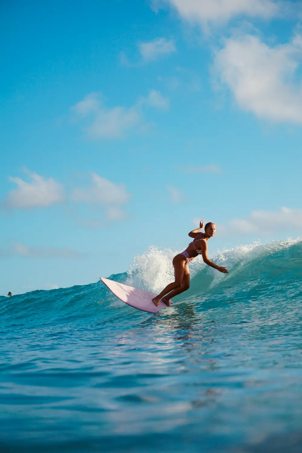 woman riding a pink surfboard along a bright blue wave under a sunny sky, image for surfing captions for instagram