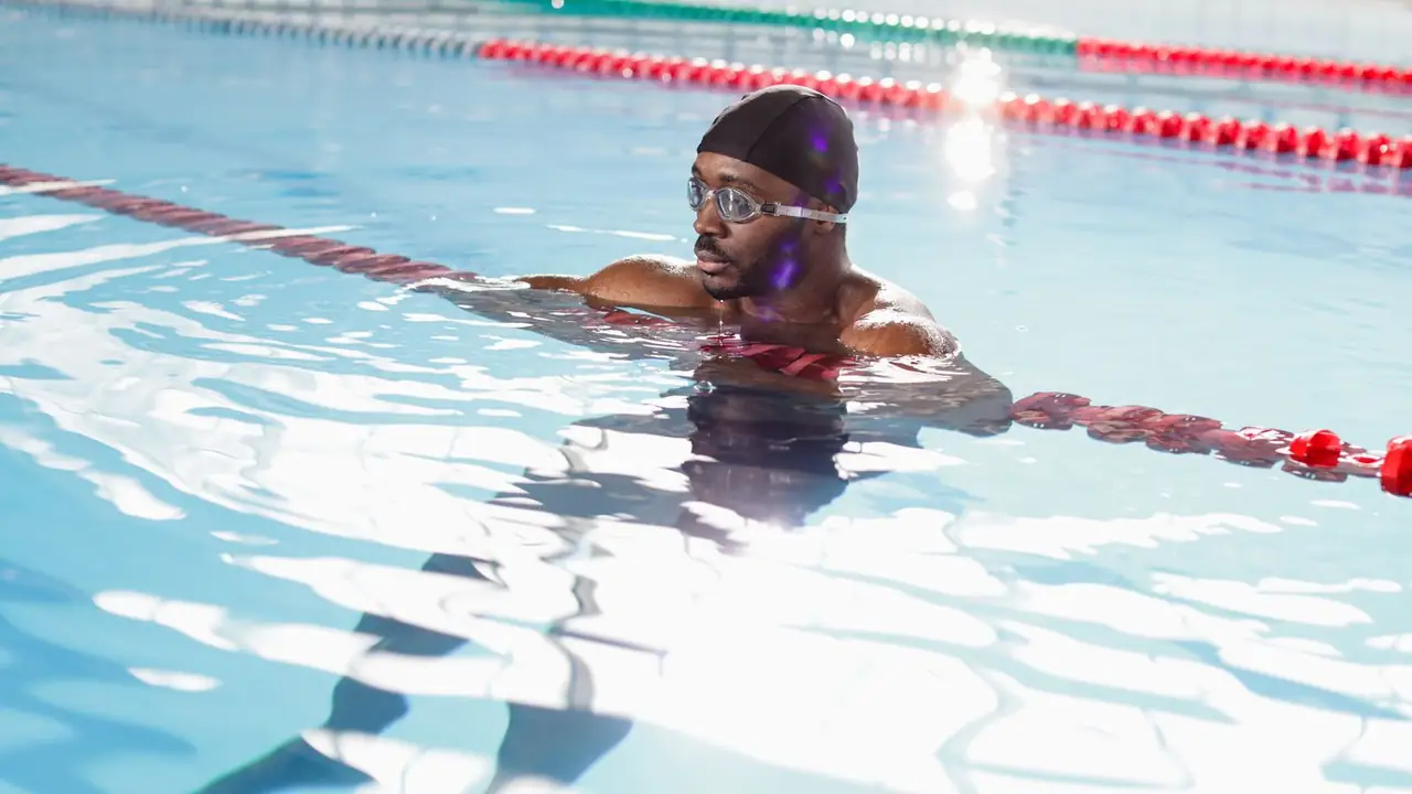a swimmer resting by red lane ropes in a bright pool, image for swim lesson and lifeguard dad jokes