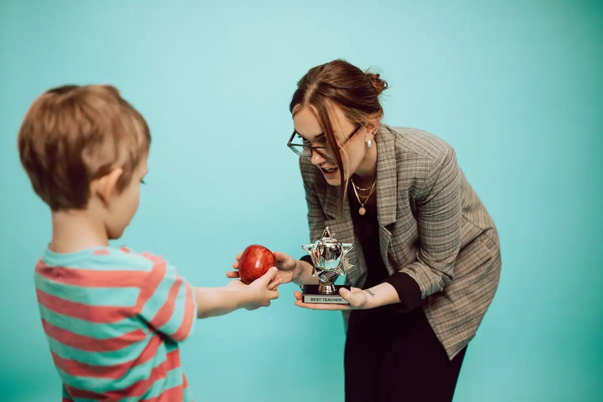 boy handing a red apple to his teacher, teacher appreciation jokes for cards