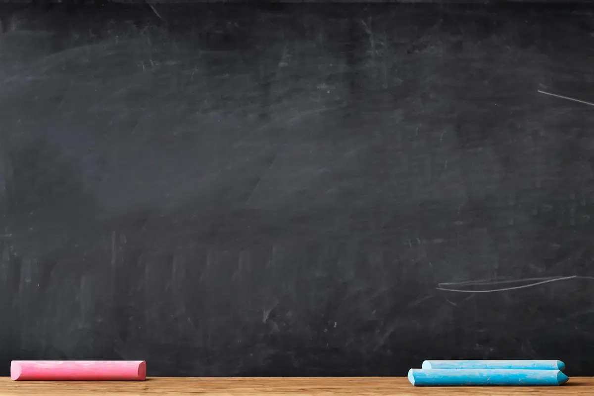 pink and blue chalk resting on a blackboard ledge, scene for short teacher puns