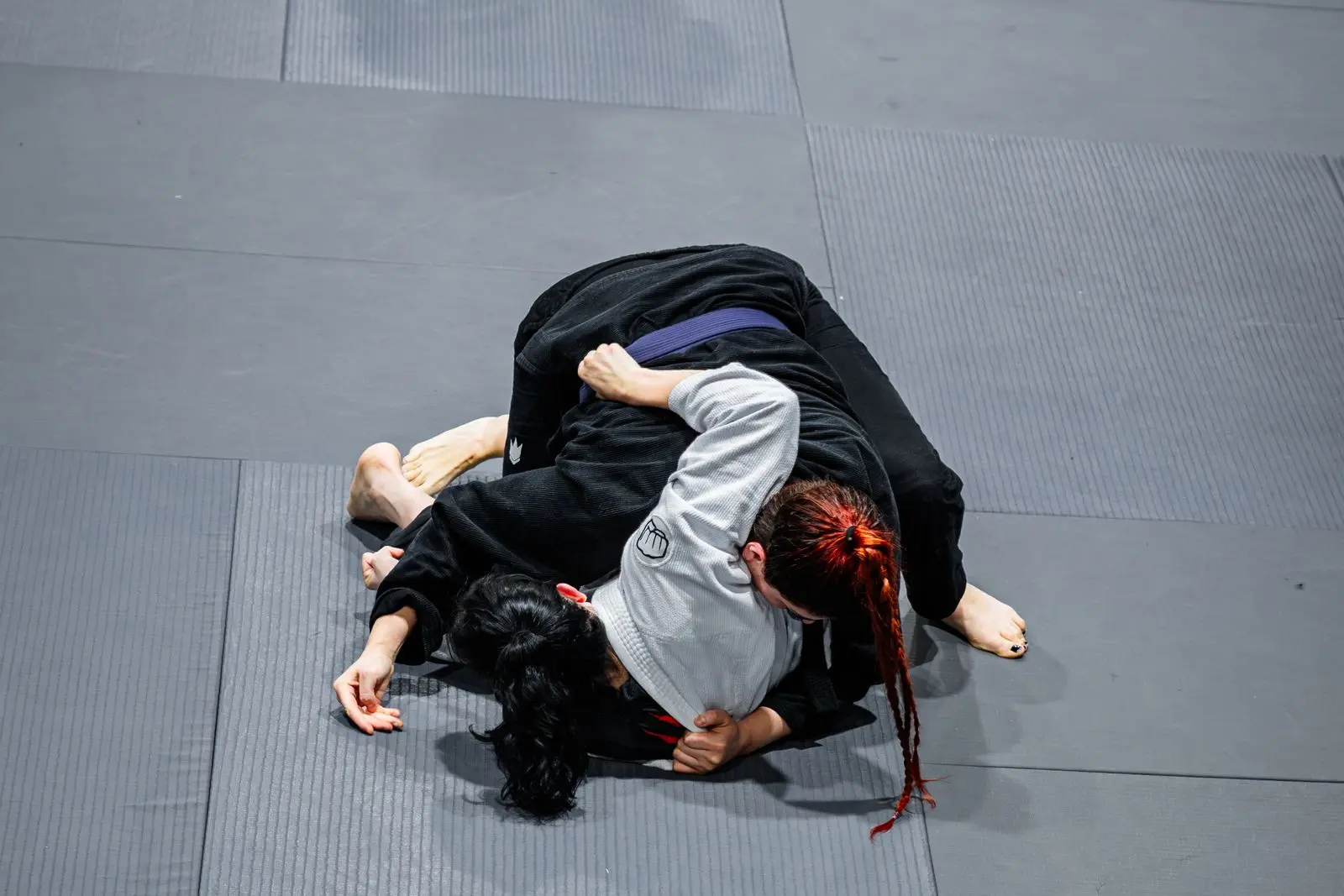 athletes competing in a grappling match on a gym mat, image for wrestling dad jokes about takedowns and pins